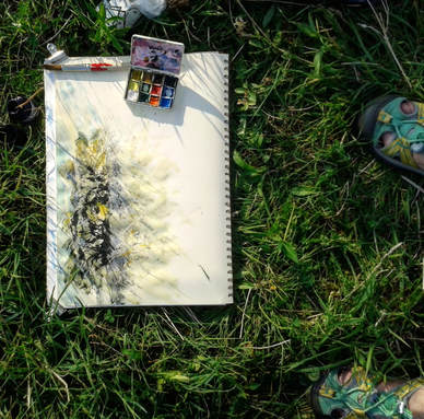 Annie's artwork in progress on a sketching trip. Picture of sketch in a meadow with paintbox and brush